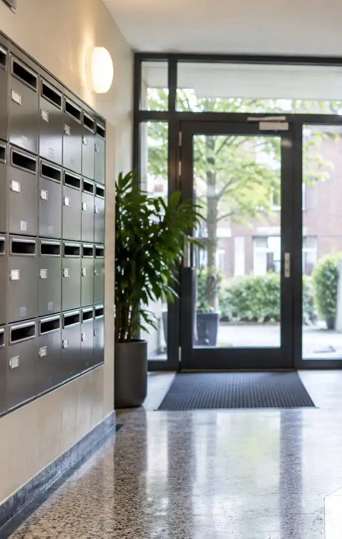 Schone entree van een VvE-complex met brievenbussen, een plant en een deurmat